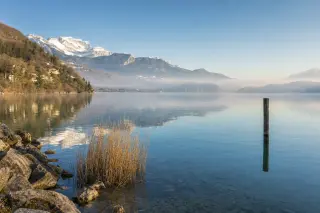 Serene Lac d’Annecy with mountain reflections, spring morning mist, and muted alpine colors.