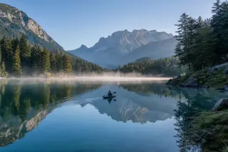Lake Annecy at dawn with light mist over the water, a single kayak gliding quietly, pine trees on the shoreline, and distant Aravis mountains under soft morning light.